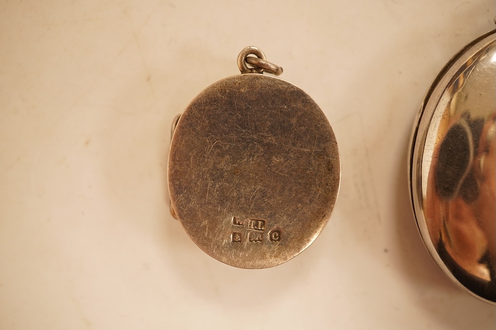 A late Victorian embossed and engraved oval silver locket, 42mm, on a later white meta belcher link chain, together with an Edwardian silver and hardstone inlaid pill box, now with pendant mount.